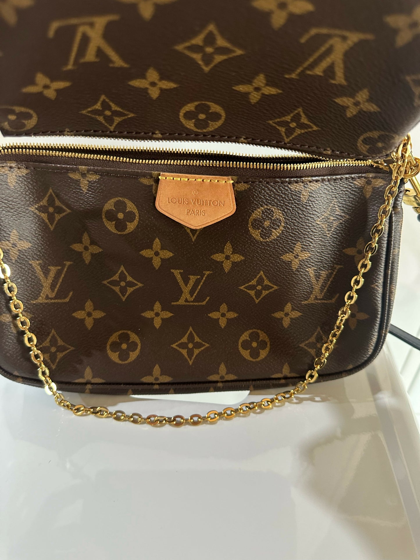 A close-up of the EXCHANGE Louis Vuitton Multi Pochette - Full Set shows the iconic monogram canvas, gold zipper, and chain strap, elegantly displayed on a white surface.