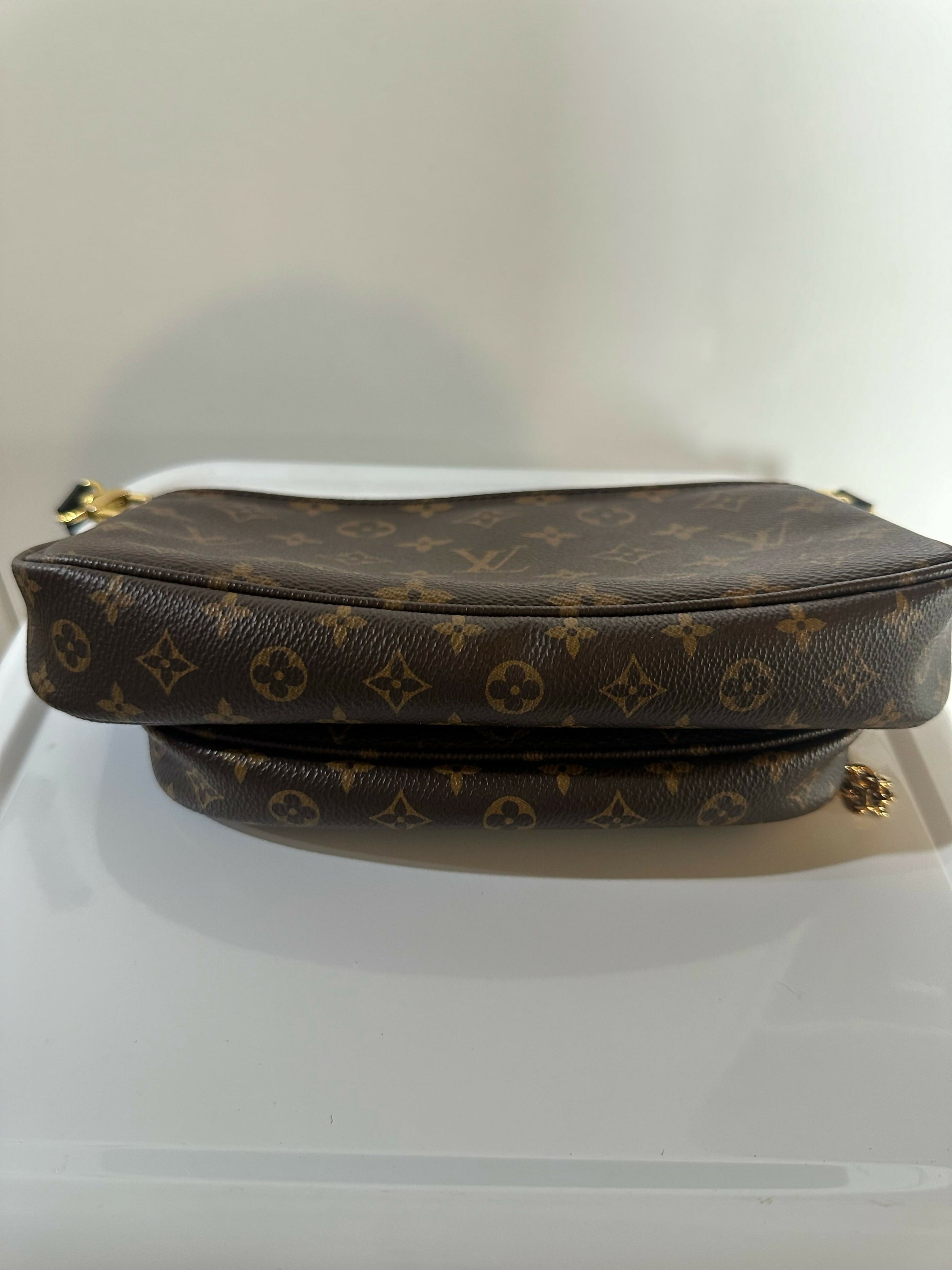 A Louis Vuitton Multi Pochette - Full Set by EXCHANGE, with signature brown monogram canvas and a black leather strap, is displayed on a white surface against a simple light background.