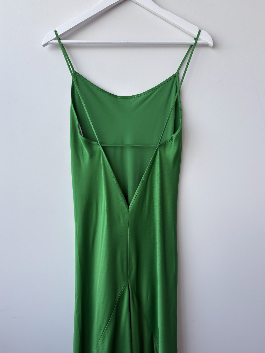 The EXCHANGE STORE Victoria Beckham Resort 2022 Green Cami Slip Dress features a sleeveless satin design with thin straps, deep V-neckline, and fitted silhouette, displayed on a white hanger against a plain white wall.