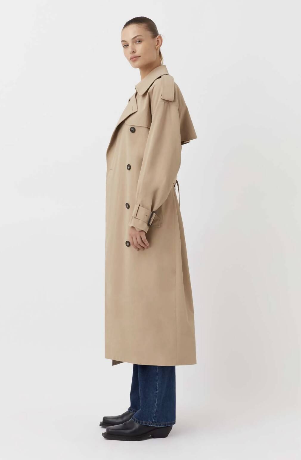 A person in profile wears an EXCHANGE Evans Trench Coat Camilla & Marc (extra small, beige) with blue jeans and black shoes against a white background. The coat has been worn once and is in great condition.
