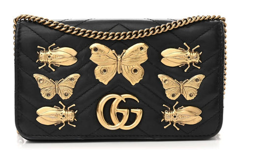 A black quilted calfskin leather Gucci Marmont Butterfly Bag by EXCHANGE, with a gold chain strap, animal studs, gold butterfly and bee embellishments, and a bold double-G logo on the front.