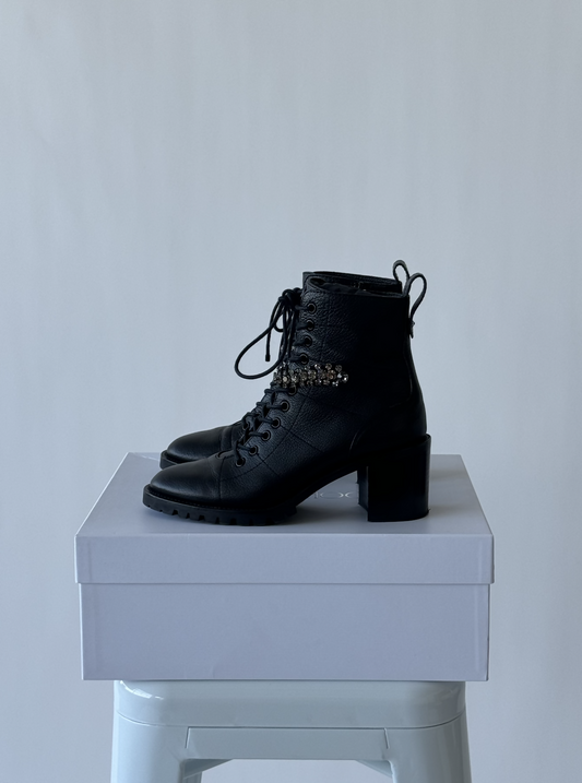 The Jimmy Choo Black Lace Up Bejewelled Strap Boots - FULL SET by EXCHANGE are displayed on a closed white box against a light gray background.