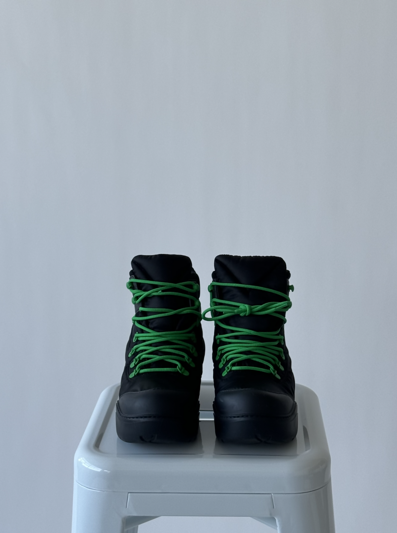 A pair of EXCHANGE Bottega Veneta Puddle Lace Up Boots in black with bright green laces, size 38, are displayed side by side on a white stool against a plain light gray background.
