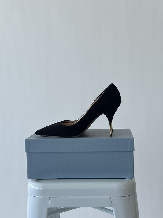 The EXCHANGE Prada Suede Pump - Gold Stiletto - Full Set in black, size 39, is displayed on a closed blue shoe box atop a white stool against a plain light gray background.