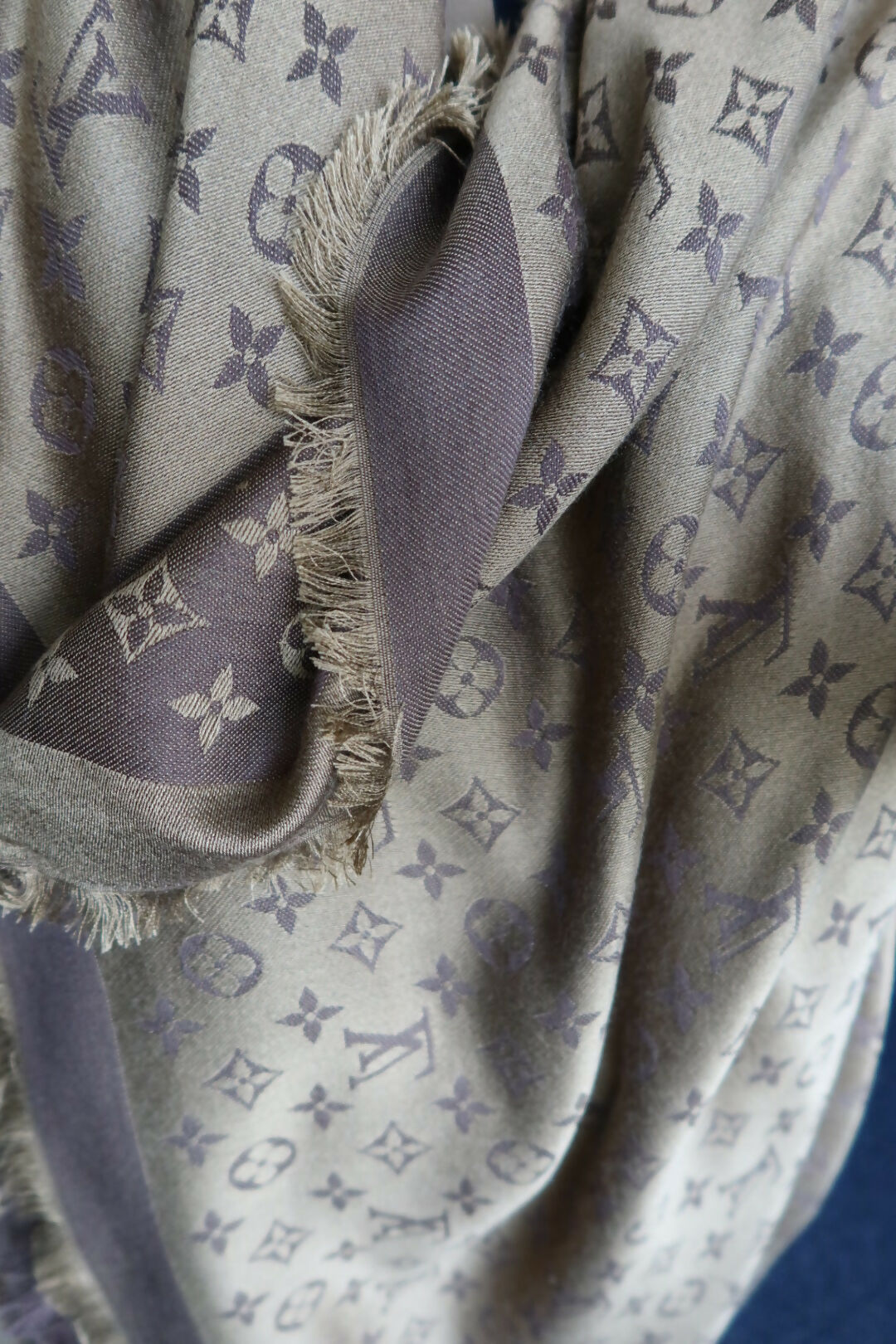 A close-up of the EXCHANGE Louis Vuitton Scarf in beige and gray, showing frayed edges and a repeating monogram with floral motifs.