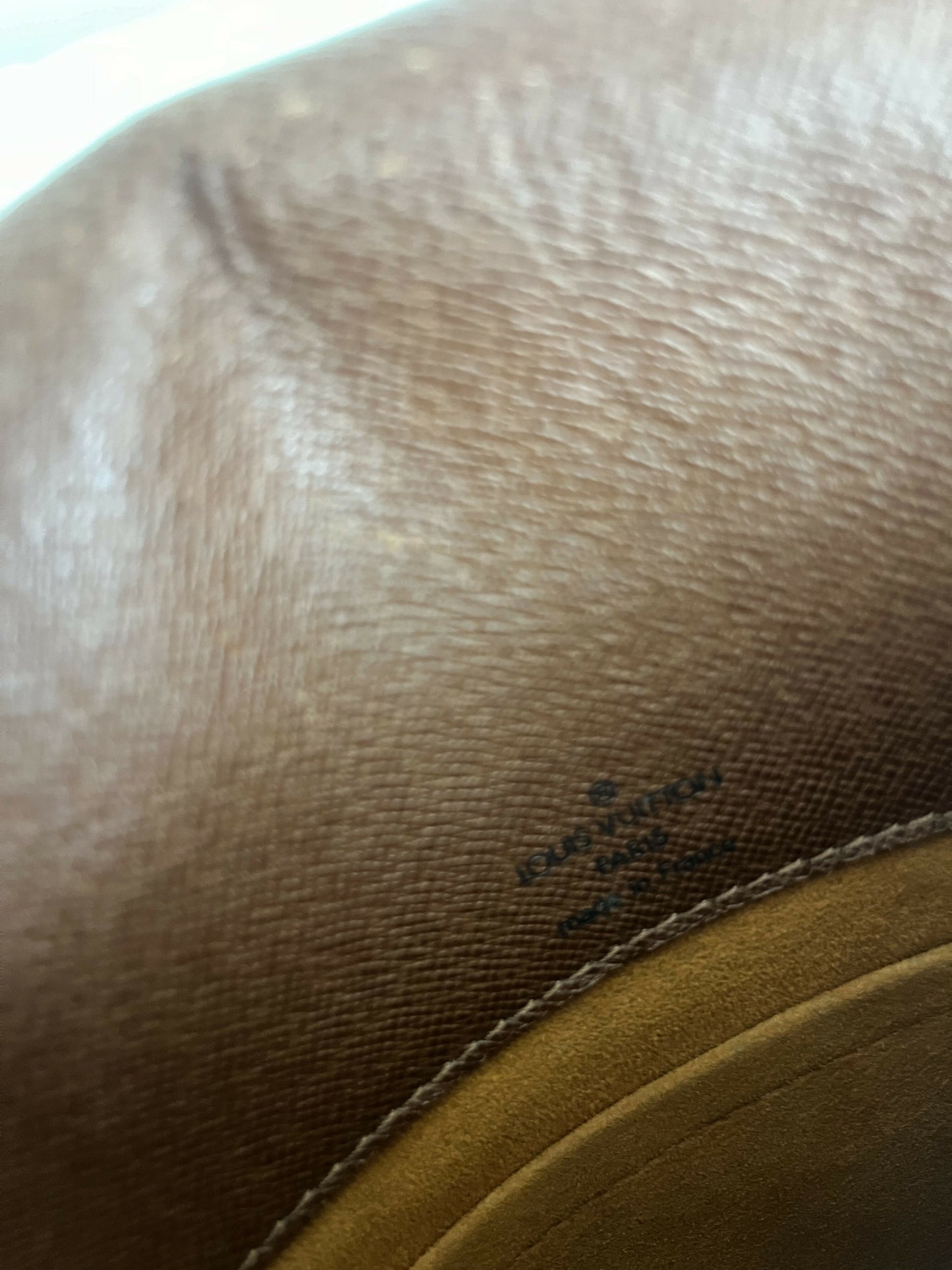 Close-up of tan leather with visible grain, stitching, and a slightly blurred black stamp. This detail highlights the quality of an authenticated Louis Vuitton Monogram Musette by EXCHANGE, available at the Exchange Store.