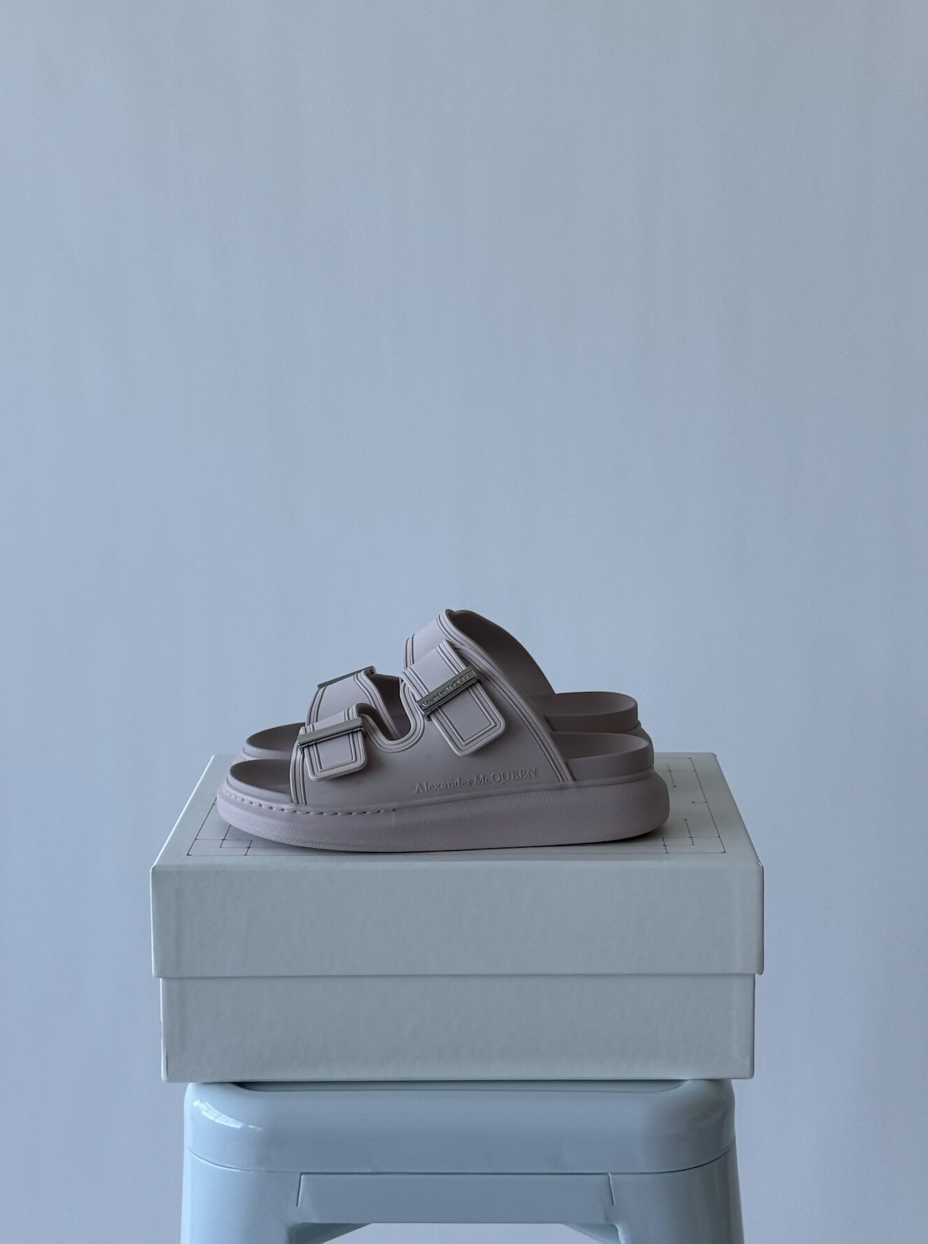 A pair of Alexander McQueen Women Hybrid slide sandals in pink/silver, size 37, with double straps and buckles by EXCHANGE are displayed on a white shoe box atop a light blue stool against a gray background. Full set: original receipt & dustbag.