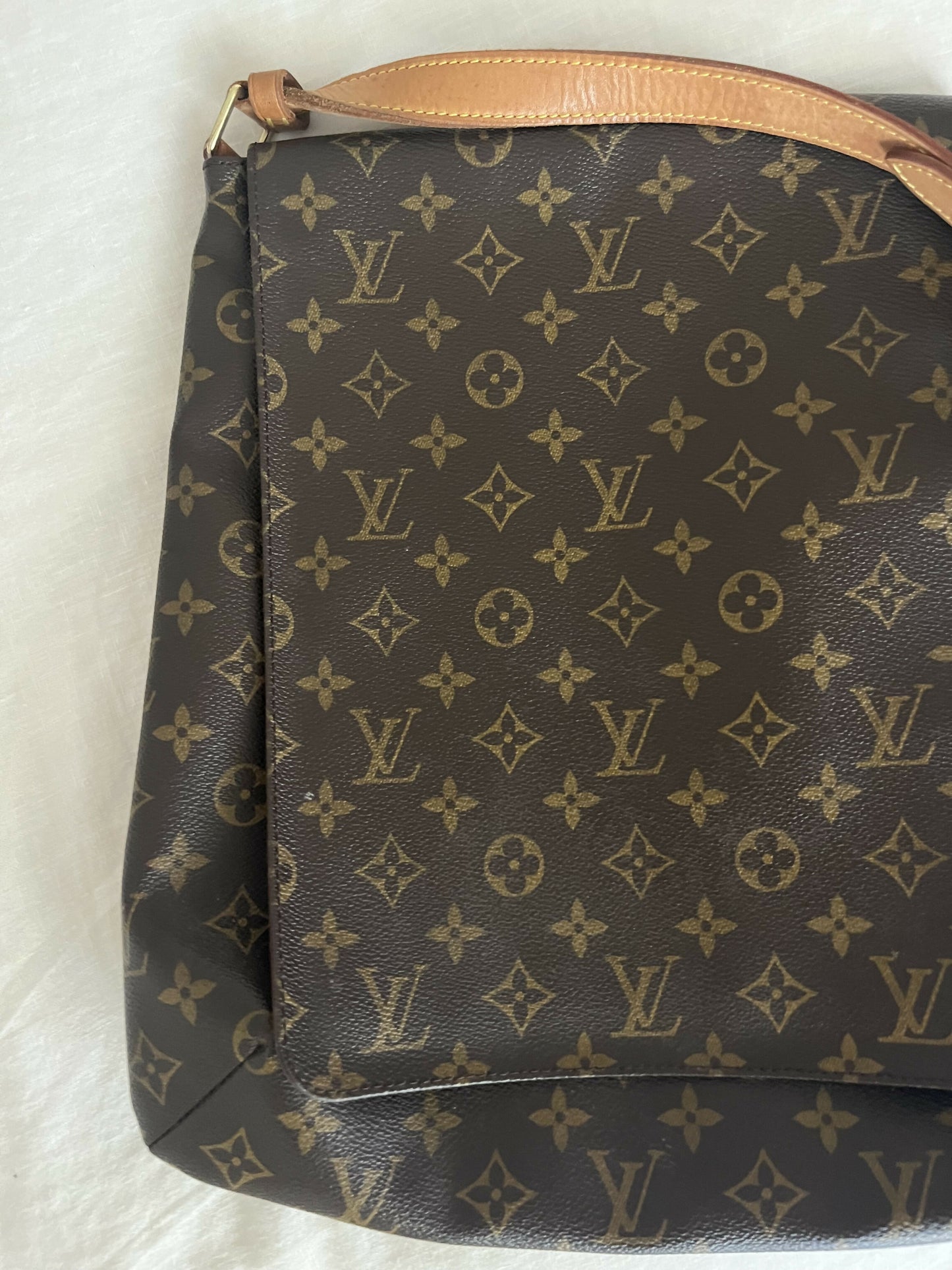 A close-up of the Louis Vuitton Monogram Musette, authenticated by EXCHANGE, shows its iconic gold LV monogram and tan leather strap. This used designer handbag is displayed on a light surface—ideal for any EXCHANGE collection.