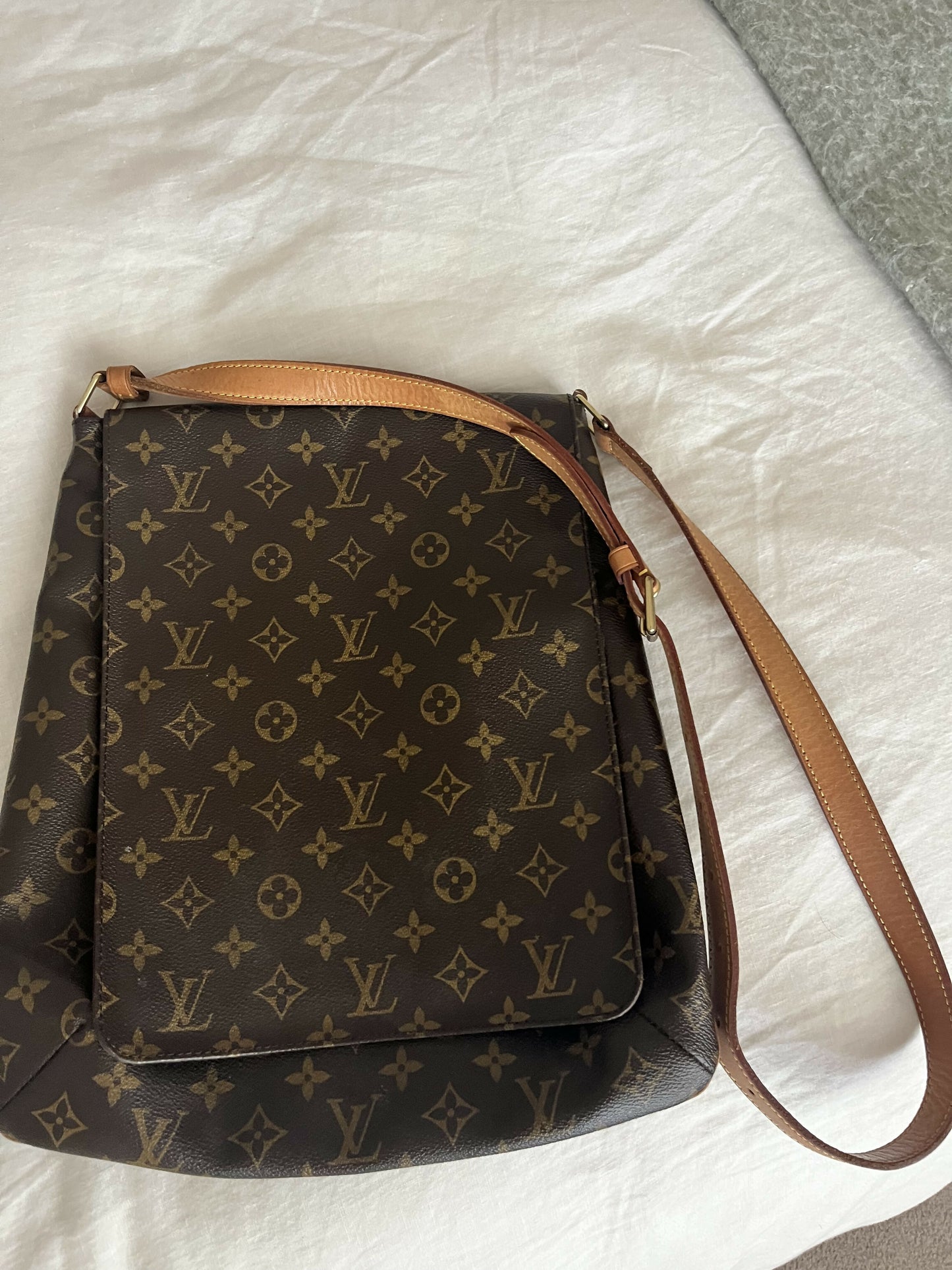 The Louis Vuitton Monogram Musette, with classic brown canvas and tan leather strap, rests on a white bedsheet—an authenticated handbag from EXCHANGE.