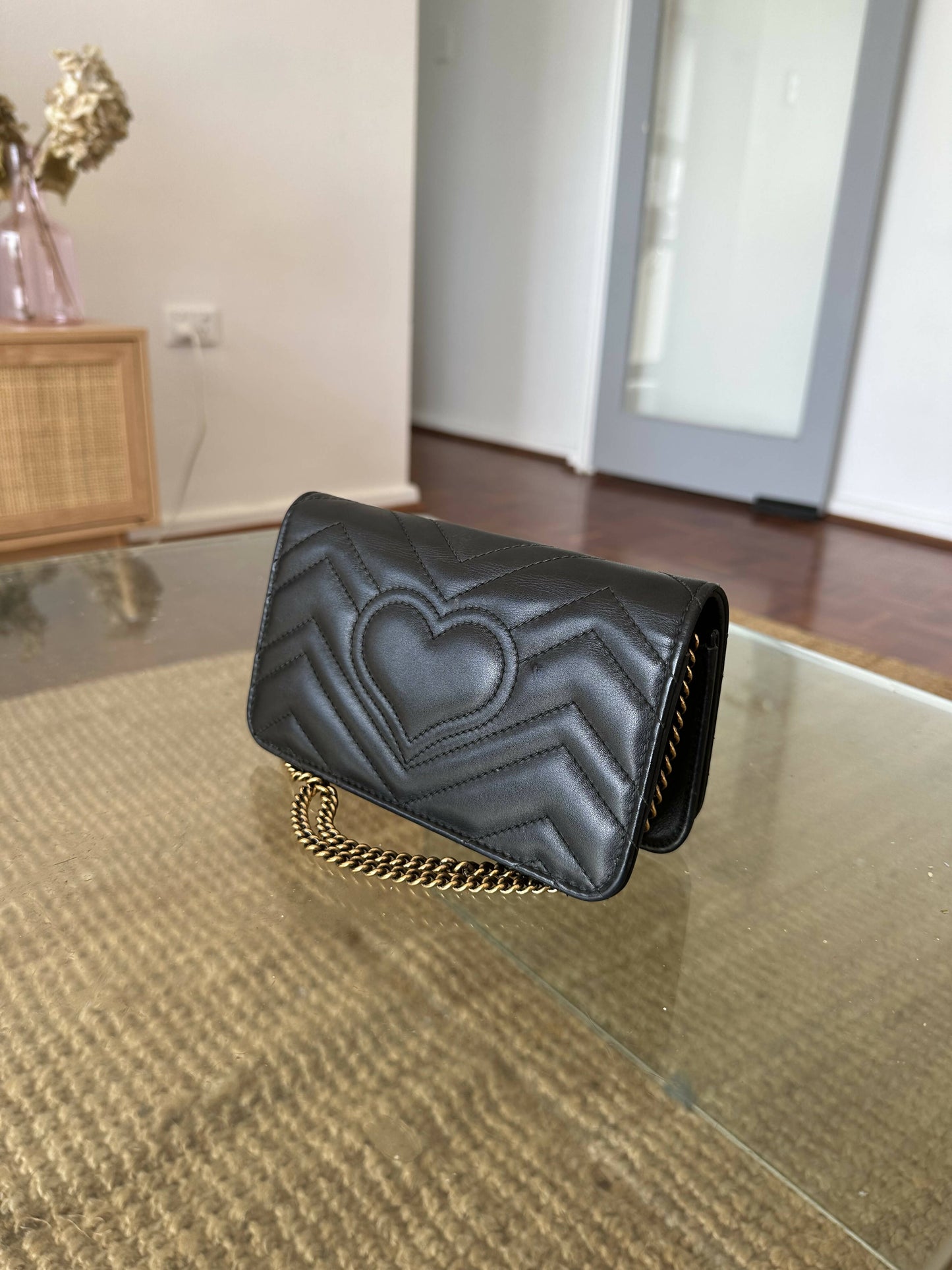 An EXCHANGE Gucci Marmont Butterfly Bag rests on a glass coffee table in a modern living room.