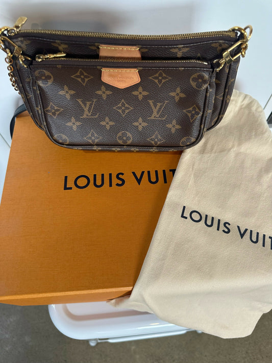 The EXCHANGE Louis Vuitton Multi Pochette - Full Set with gold accents rests on an orange box beside a beige dust bag, showcasing the classic brown Monogram canvas and a chic black leather strap.