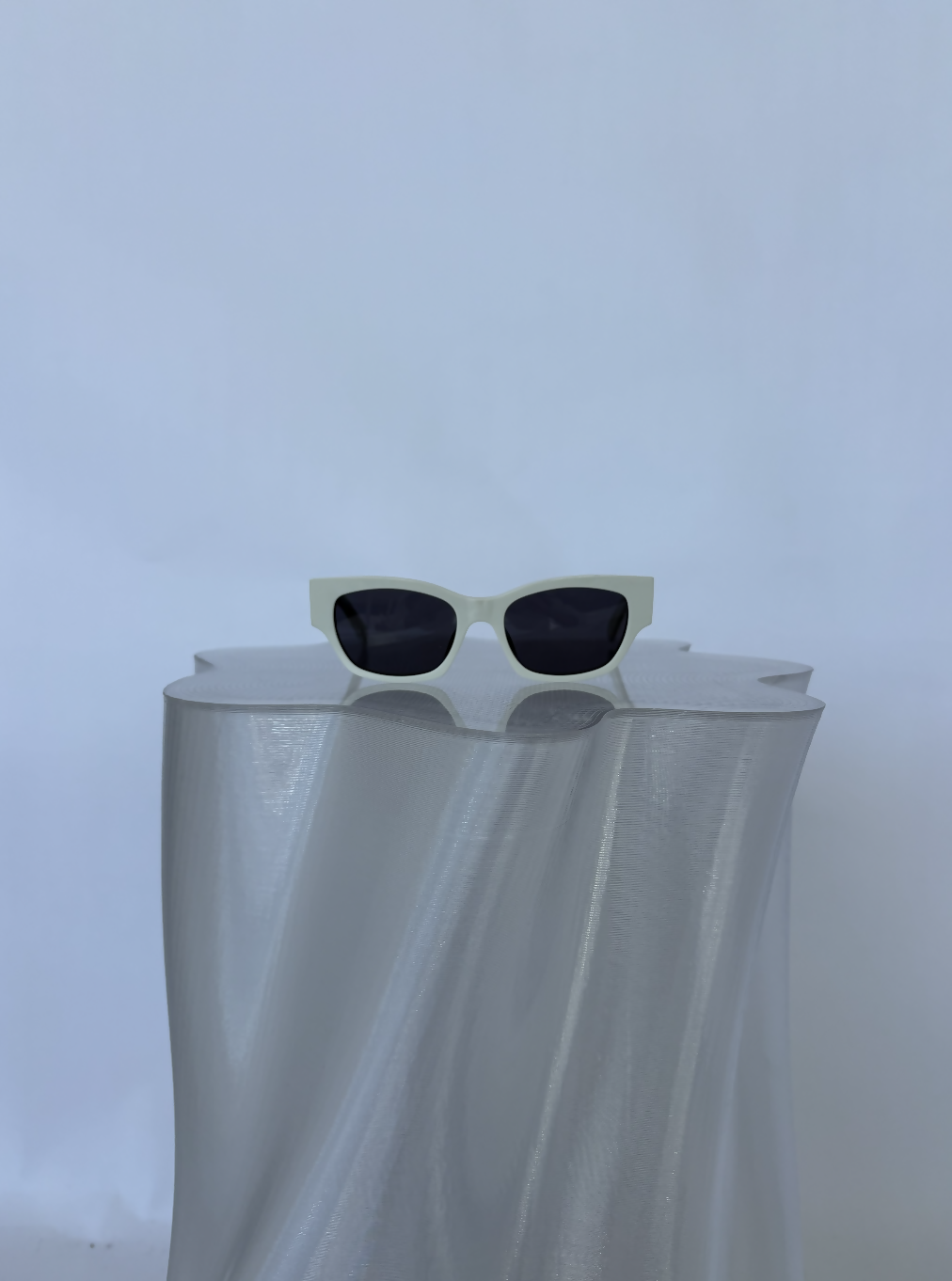 A pair of Celine Beige Sunglasses from EXCHANGE STORE, featuring a beige frame and dark lenses, is displayed on a sculpted metallic silver pedestal against a plain, light background.