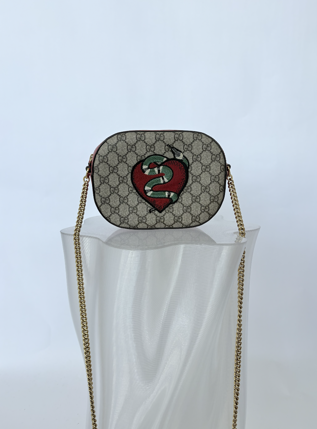 The EXCHANGE STORE Gucci Kingsnake Heart Mini GG Supreme Chain Crossbody Bag - FULL SET is displayed on a translucent sculpted stand against a white background.