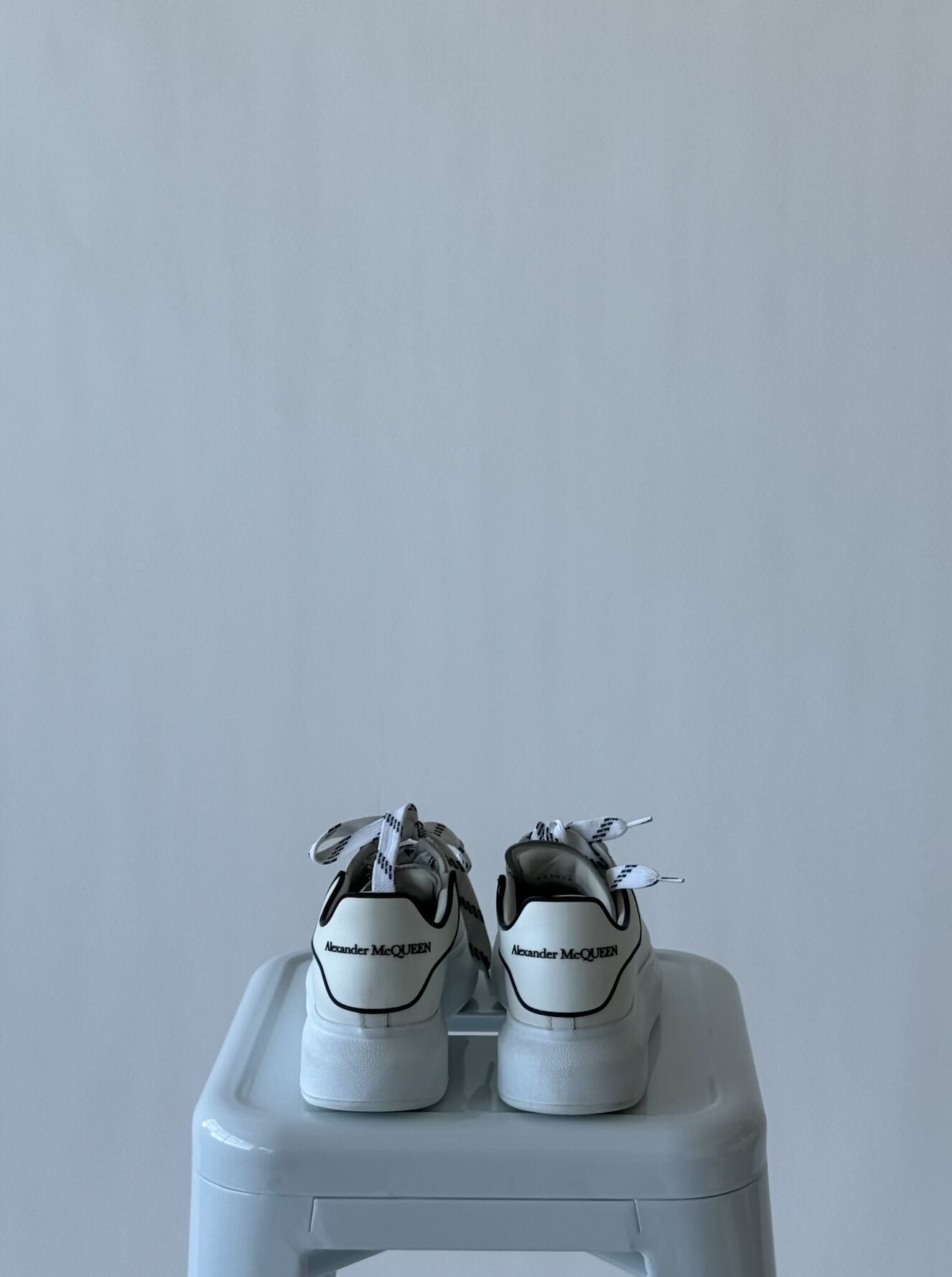 A pair of EXCHANGE Alexander McQueen Oversized White Black Trim sneakers, size 37, are side by side on a light gray stool against a plain background. Includes dust bag for a complete set.