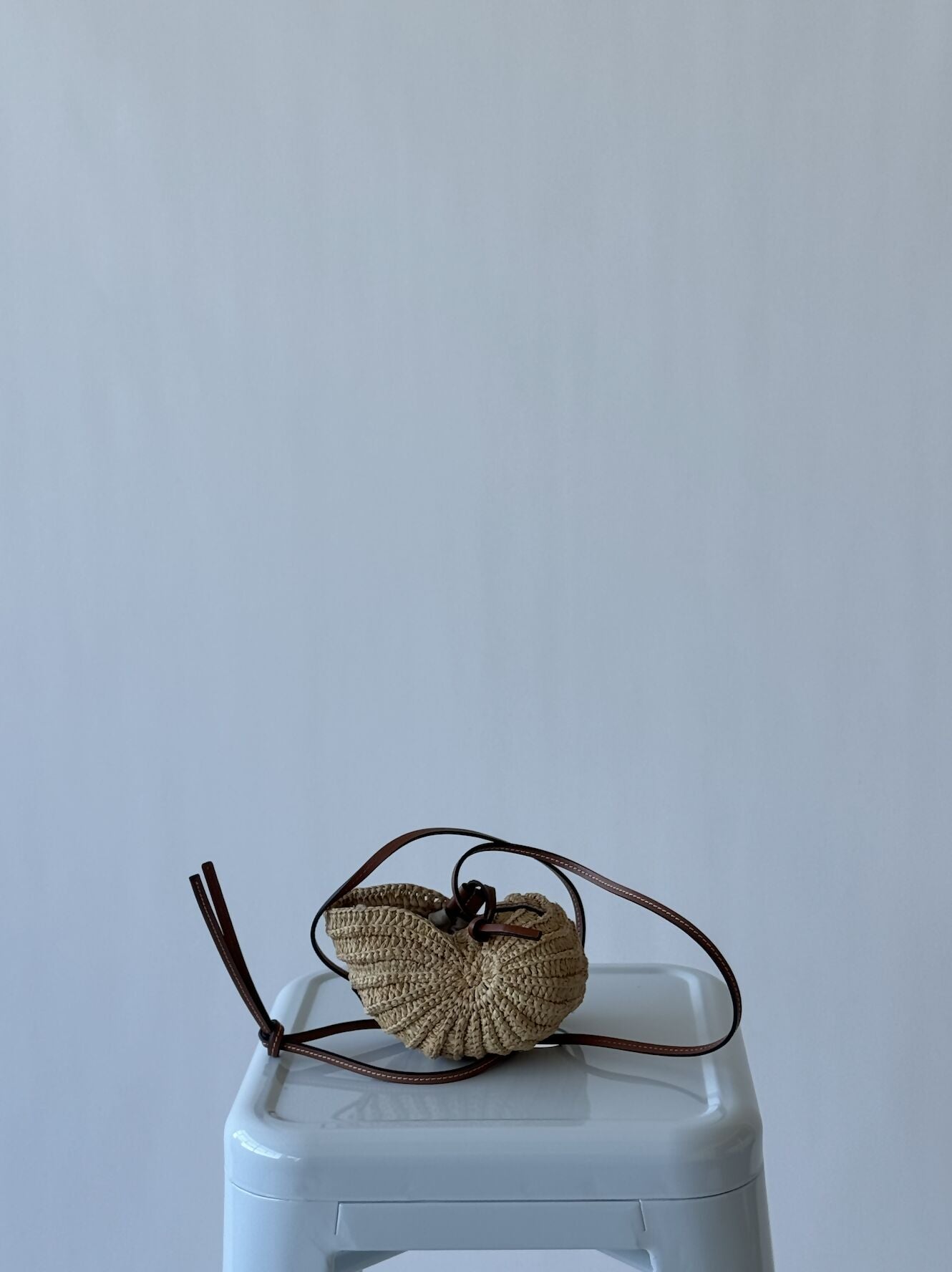 A LOEWE - Cross body shell bag from EXCHANGE, in excellent condition with a dark brown leather strap, sits on a pale gray plastic stool against a light gray background.