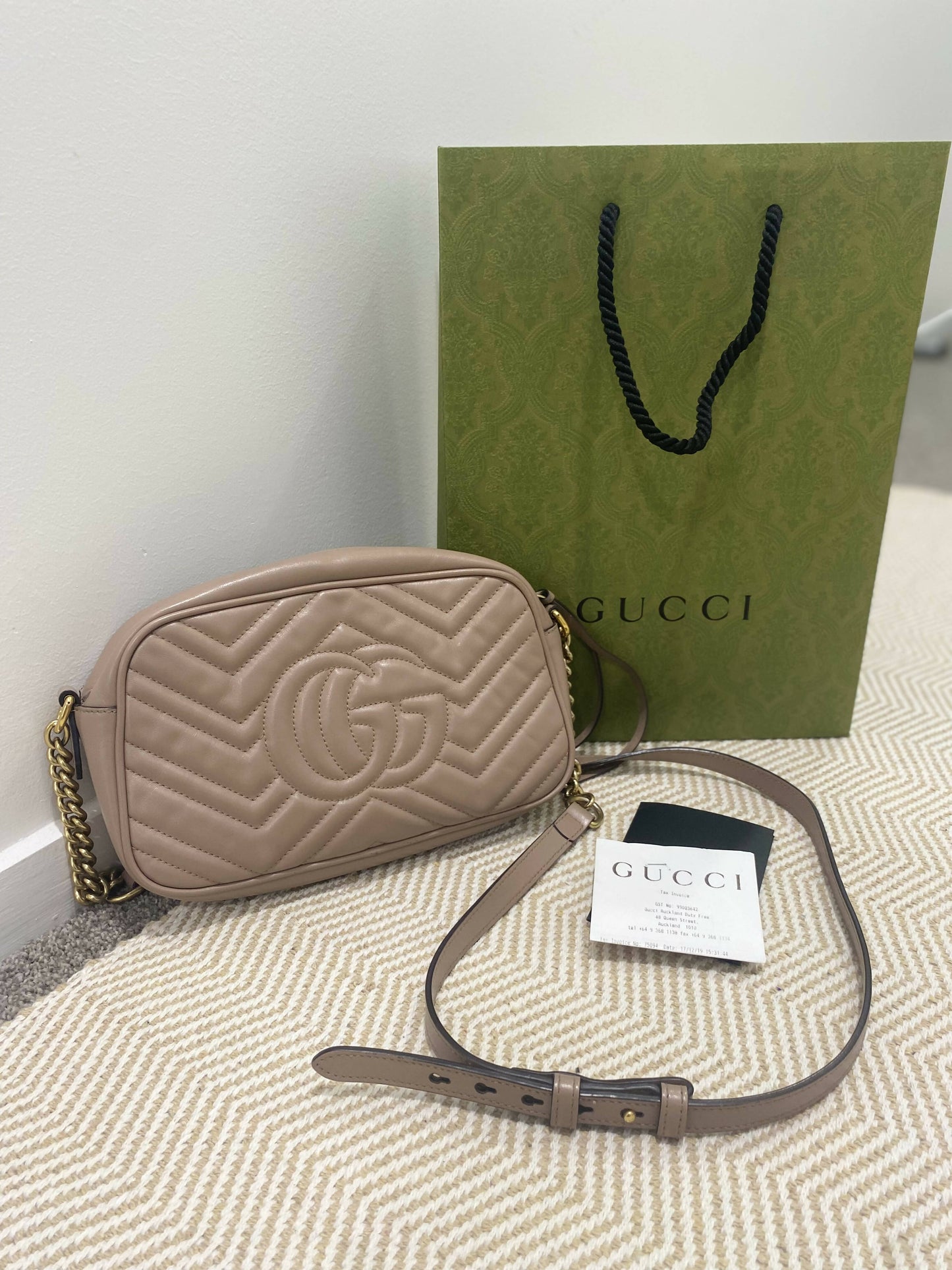 The Gucci Marmont Matelasse Small Dusty Pink by EXCHANGE is displayed on a beige patterned surface with a green shopping bag, authentication cards, and a dustbag.