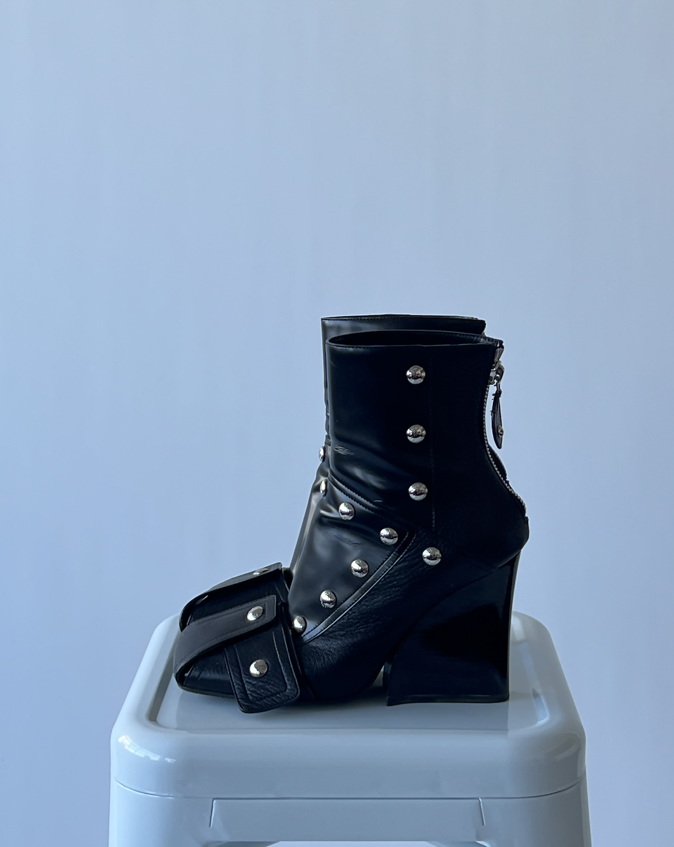 A black high-heeled ankle boot with silver studs and buckles from the EXCHANGE LV Fall Winter 2021-2022 - Full Set, displayed on a white stool against a light background.