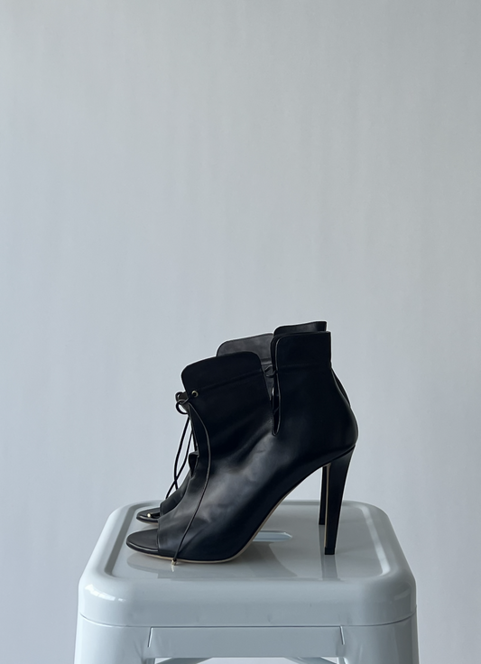 A pair of EXCHANGE Jimmy Choo - Murphy leather heel ankle boots with open toes and lace-up fronts, shown side by side on a white stool against a light gray background.