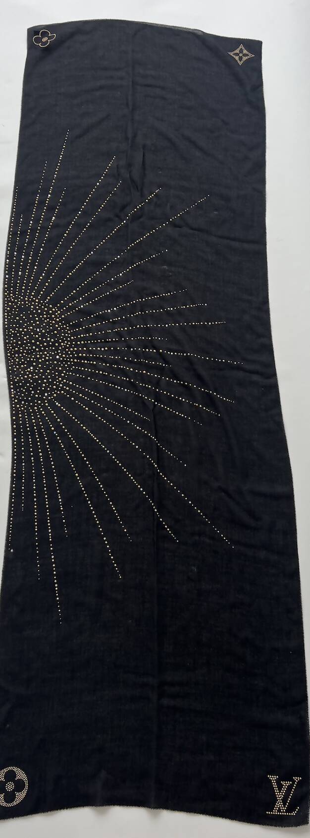 The EXCHANGE Louis Vuitton Cashmere Scarf is long and black, featuring a gold dotted sunburst design on one side and gold embroidered Louis Vuitton symbols in each corner. The background is plain white.
