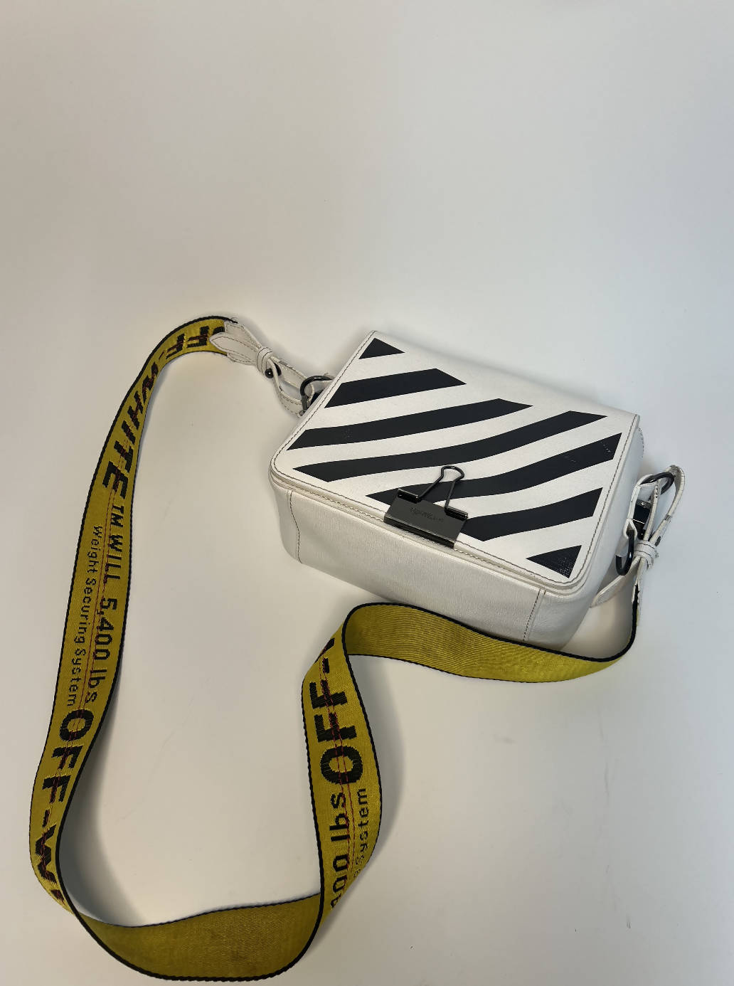 A white rectangular EXCHANGE Off-White diagonal stripe crossbody bag featuring black diagonal stripes and a wide yellow strap, displayed on a plain white background.