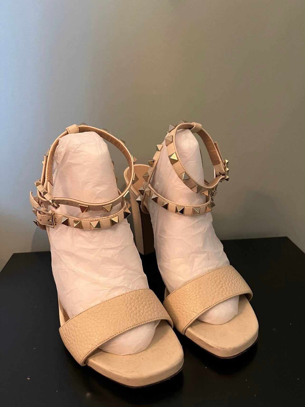 A pair of beige EXCHANGE Rock Studded Sandal - Ankle Strap Platform 39.5 women's shoes with open toes and gold studded ankle straps, displayed on a black surface with white tissue paper, reflecting platform elegance.