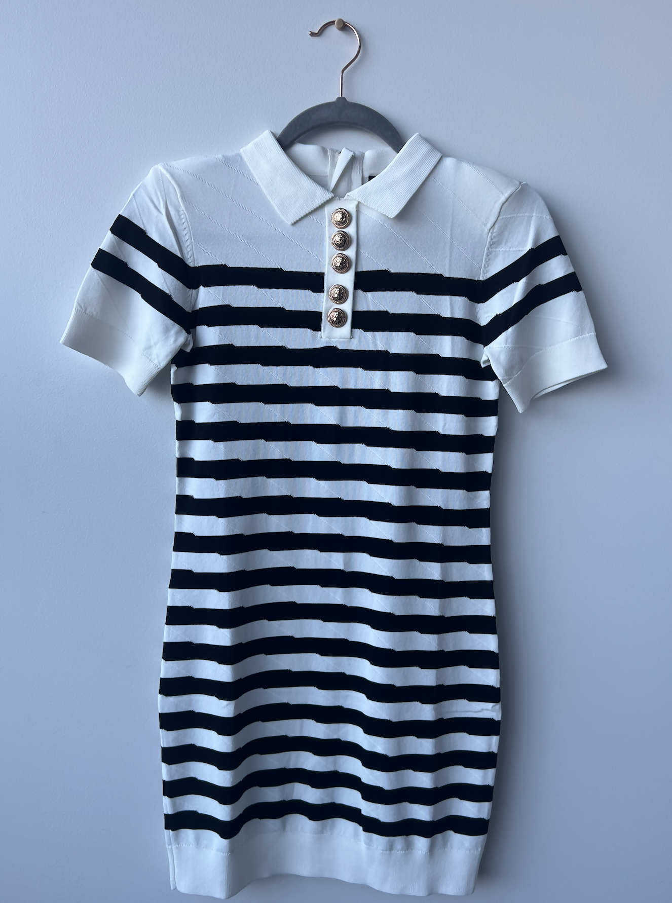 A new with tags, short-sleeved EXCHANGE Balmain Dress in size 36 features black and white horizontal stripes, a white collar, and a five-button placket. Shown hanging on a black hanger against a light gray wall.