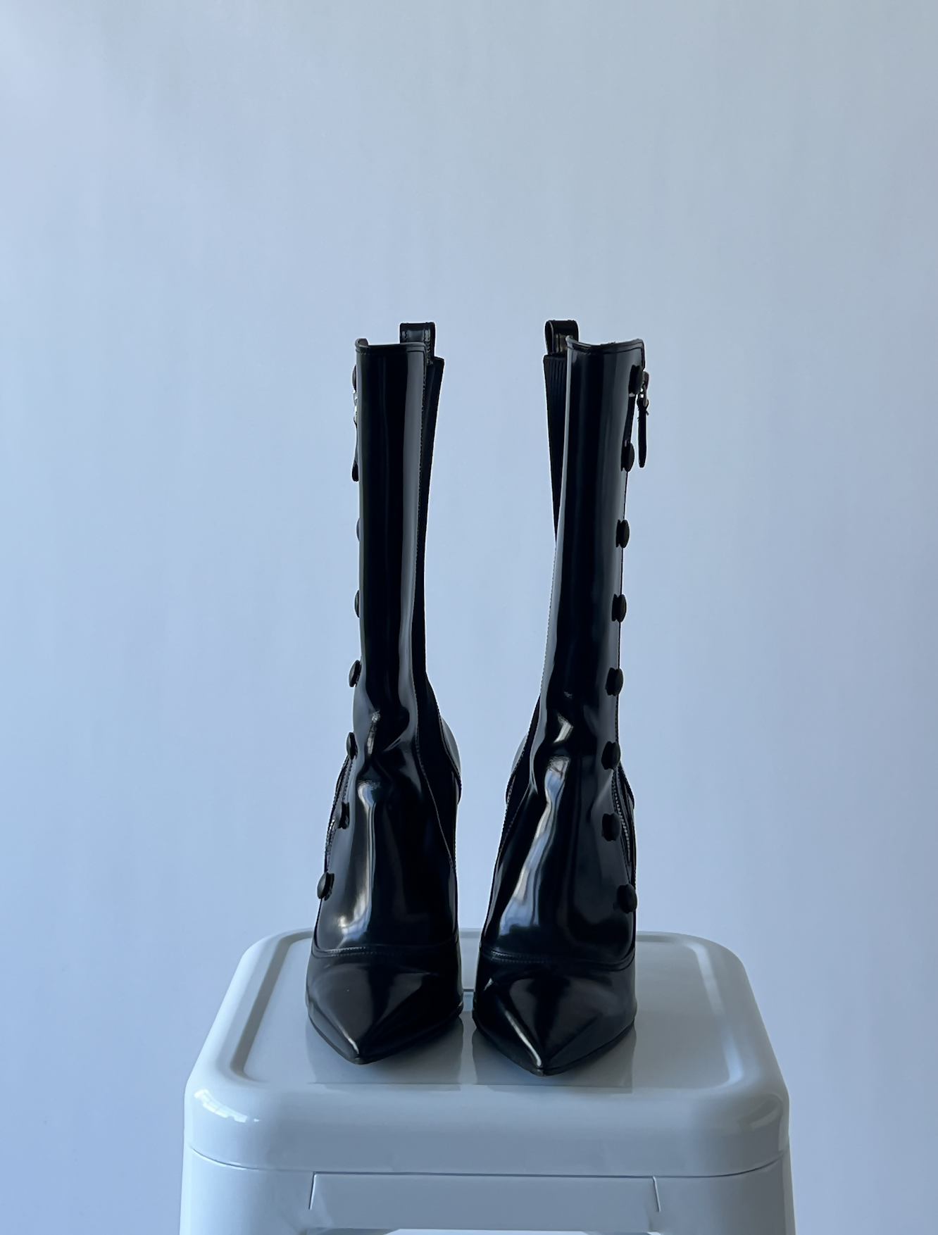 A pair of Alexander Macqueen Leather boots by EXCHANGE, size 41, shiny black high-heeled ankle style with pointed toes and button details, displayed on a white pedestal against a light gray background. Like new.