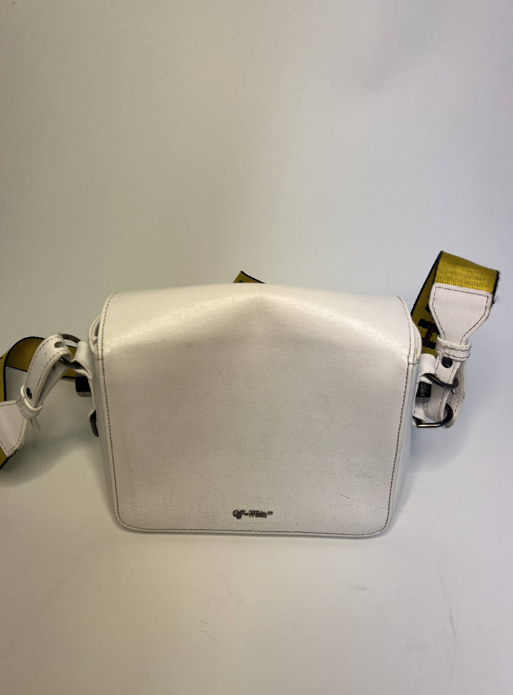 The EXCHANGE Off-White diagonal stripe crossbody bag features a textured surface, yellow adjustable strap, and small front logo, capturing Virgil Abloh’s design style. Displayed against a plain white background.
