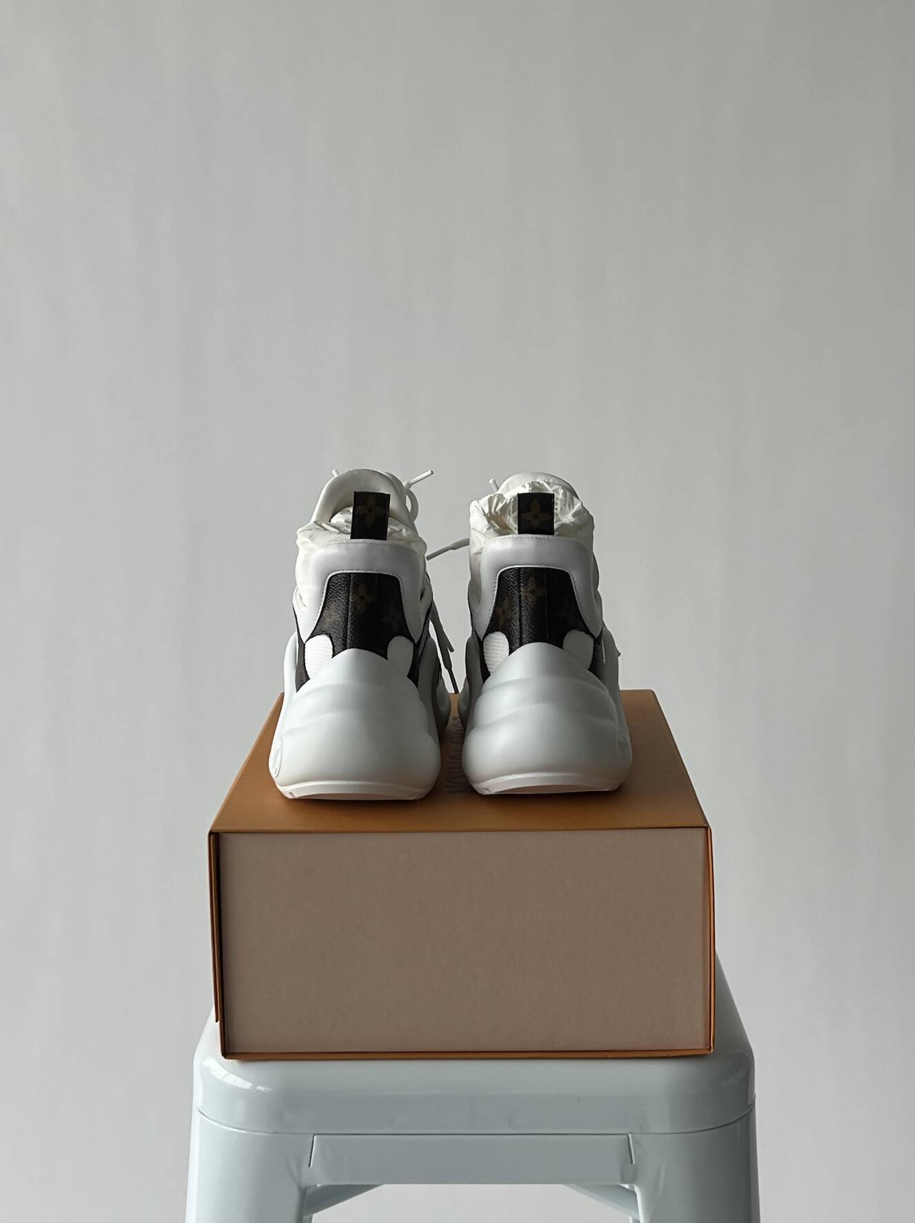 A pair of LV Archlight Sneakers by EXCHANGE, white and black, size 38, are displayed side by side on a closed brown shoe box atop a white stool against a plain light background. Never worn; in fantastic condition.
