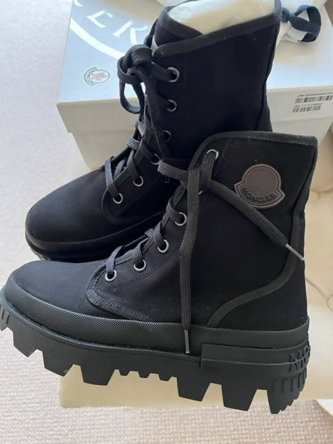 A pair of Lulu Moncler Pyla Canvas Boots—brand new, black lace-up style with chunky lugged soles (Size 40, SALE $500)—are displayed near a Moncler-branded shoe box, one upright and one resting on its side.