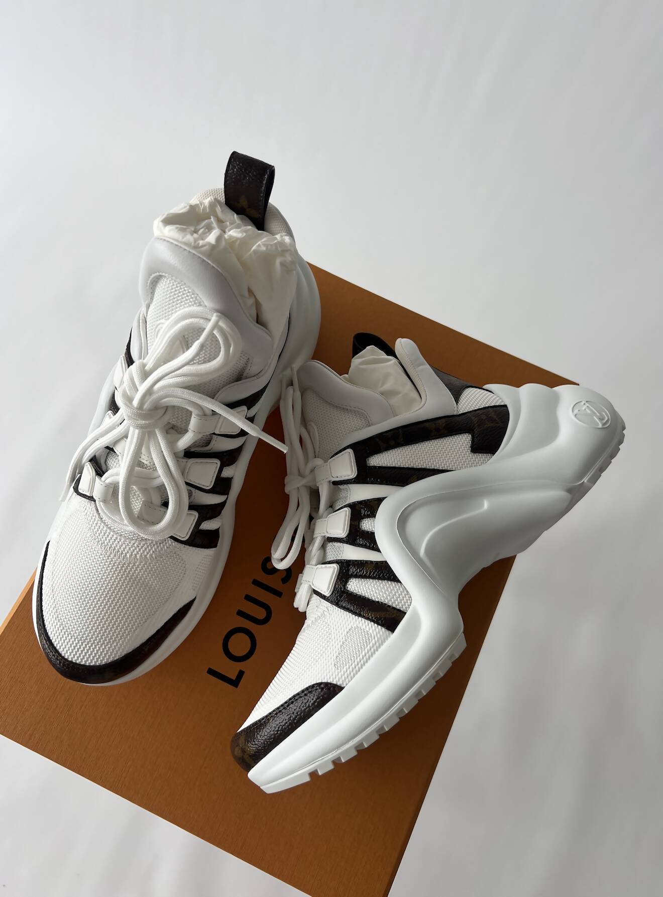 A pair of LV Archlight Sneakers by EXCHANGE in size 38, featuring chunky soles in black and white, are displayed on an orange Louis Vuitton box against a white background. These unworn, stylish shoes are in fantastic condition.