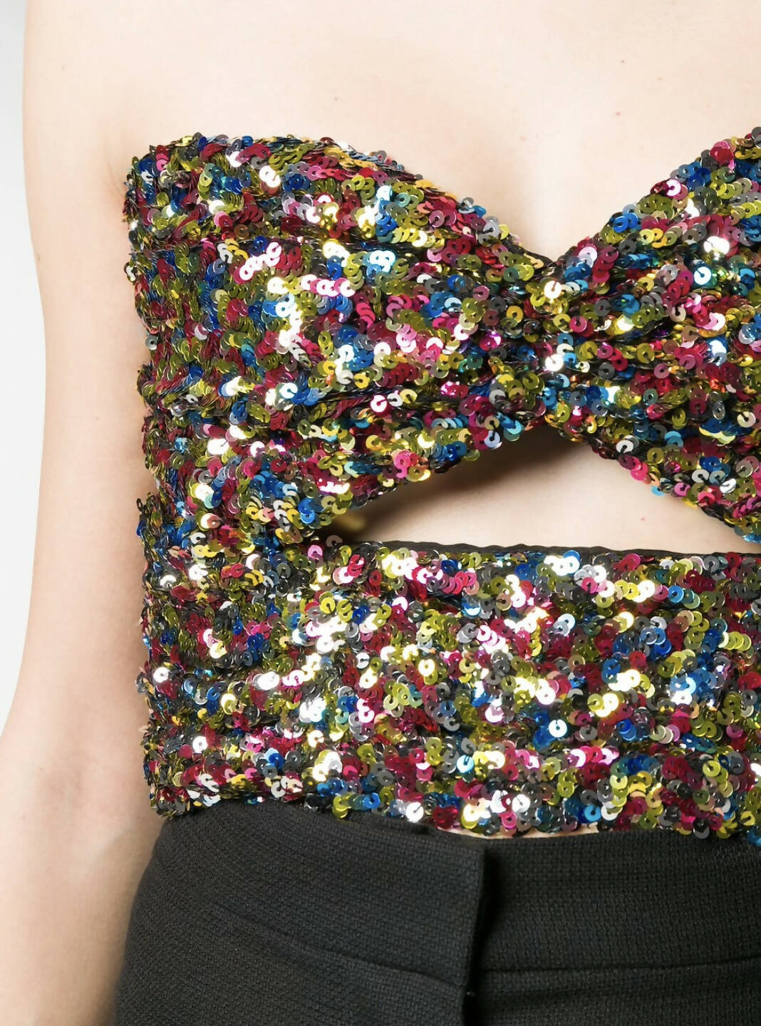 A close-up of a person wearing an EXCHANGE THE ATTICO sequinned strapless top—new with tags—featuring a front bow detail and cutout below the bust, styled with high-waisted black pants.
