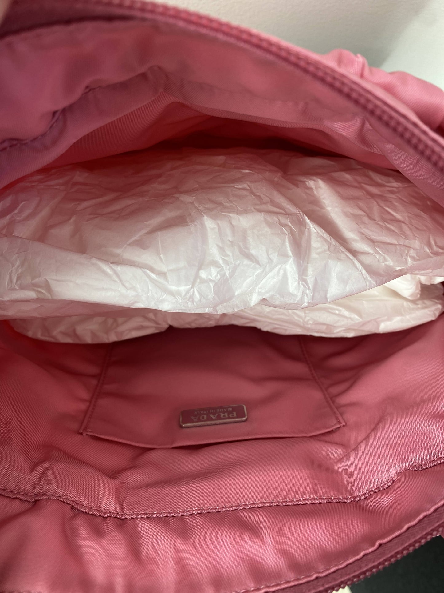 The image shows the interior of an EXCHANGE Prada Pink Nylon Tote, lined with pink fabric. A nappa leather shoulder strap, white tissue paper, and a Prada label are visible inside the bag.