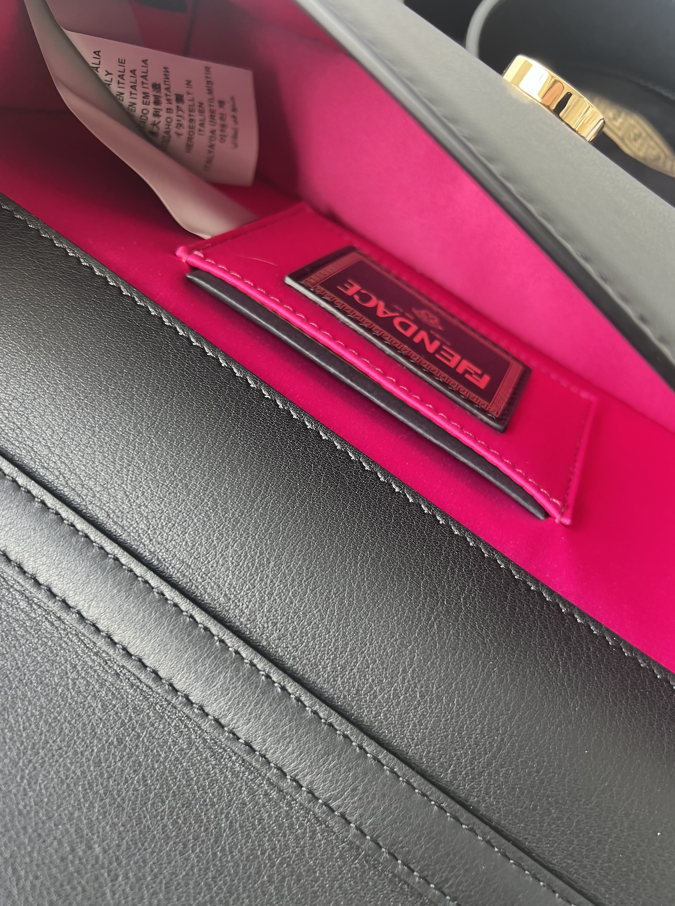 Close-up of the FENDI X Versace Fendace Baguette Shoulder Bag by EXCHANGE, featuring black leather, a bright pink interior, visible pink cardholder/label, care tag, and a gold clasp—showcasing true Italian fashion elegance.