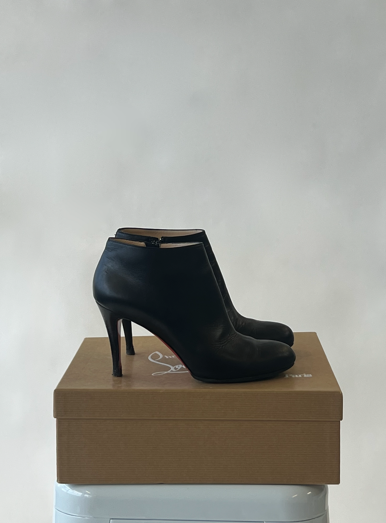 A pair of CHRISTIAN LOUBOUTIN BELLE CALF BOOT black high-heeled ankle boots by EXCHANGE, shown side by side with black soles on their original box against a plain light gray background.