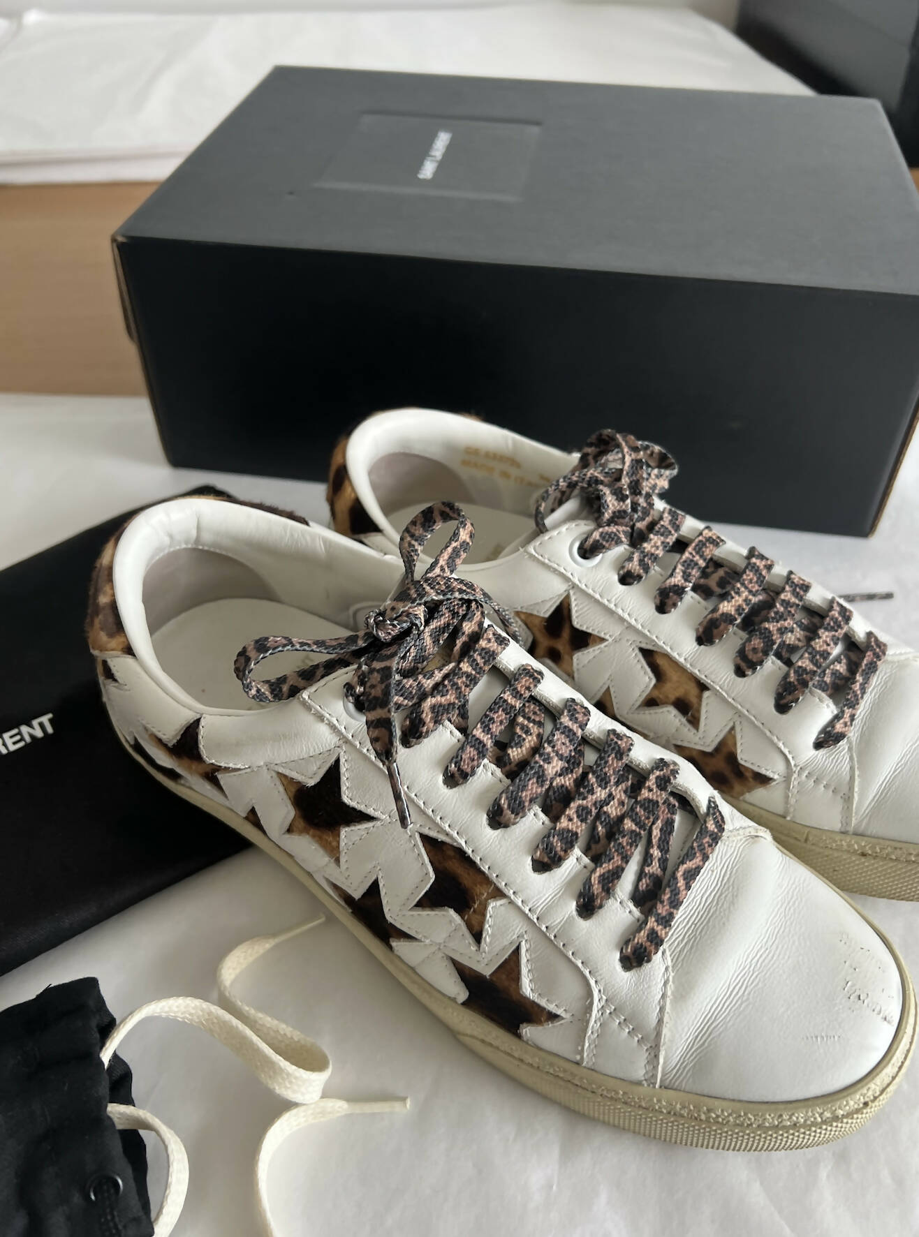 A pair of Saint Laurent Court Classic Sneakers Stars - Leopard/Cheetah sits on a white surface with a black shoebox, dust bag, and extra laces—available now at EXCHANGE in the Auckland Region.