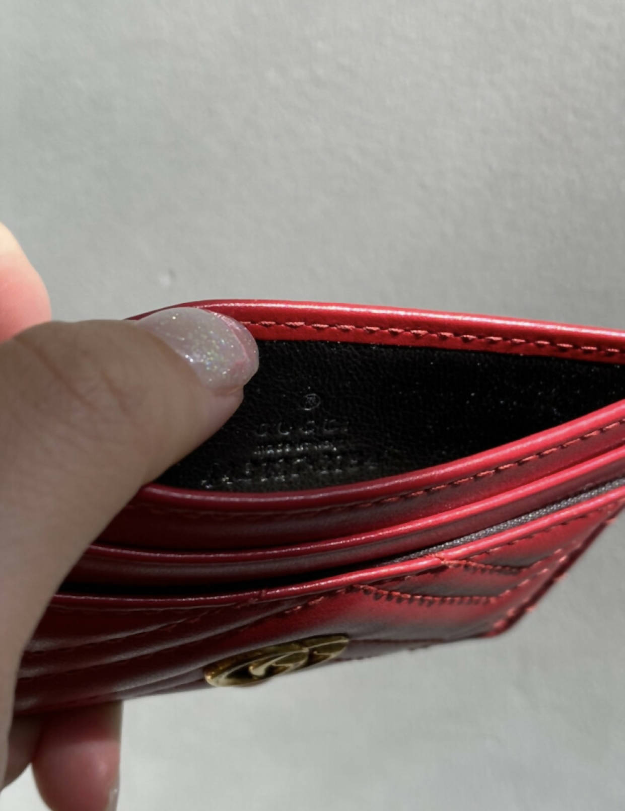 A hand with glittery polished nails holds open a slim red EXCHANGE Gucci GG Marmont Card Case, revealing its empty interior against a plain light gray background.