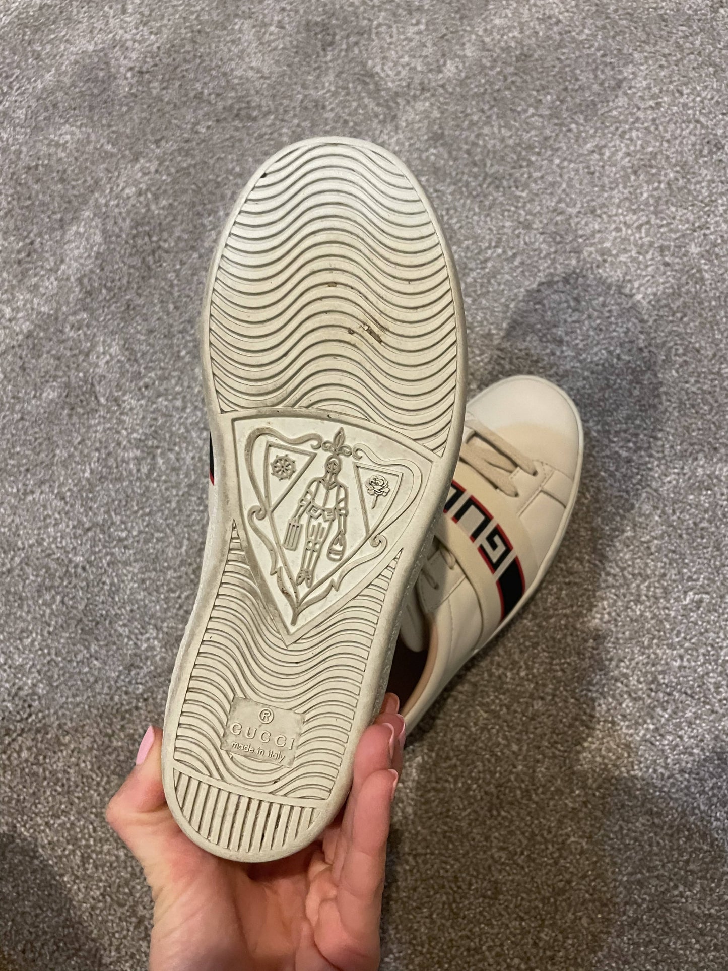 A hand displays a beige Gucci Sneaker by EXCHANGE, highlighting the embossed knight design and Gucci logo above “Made in Italy” on the sole. Available now at our Exchange store in Dubai.