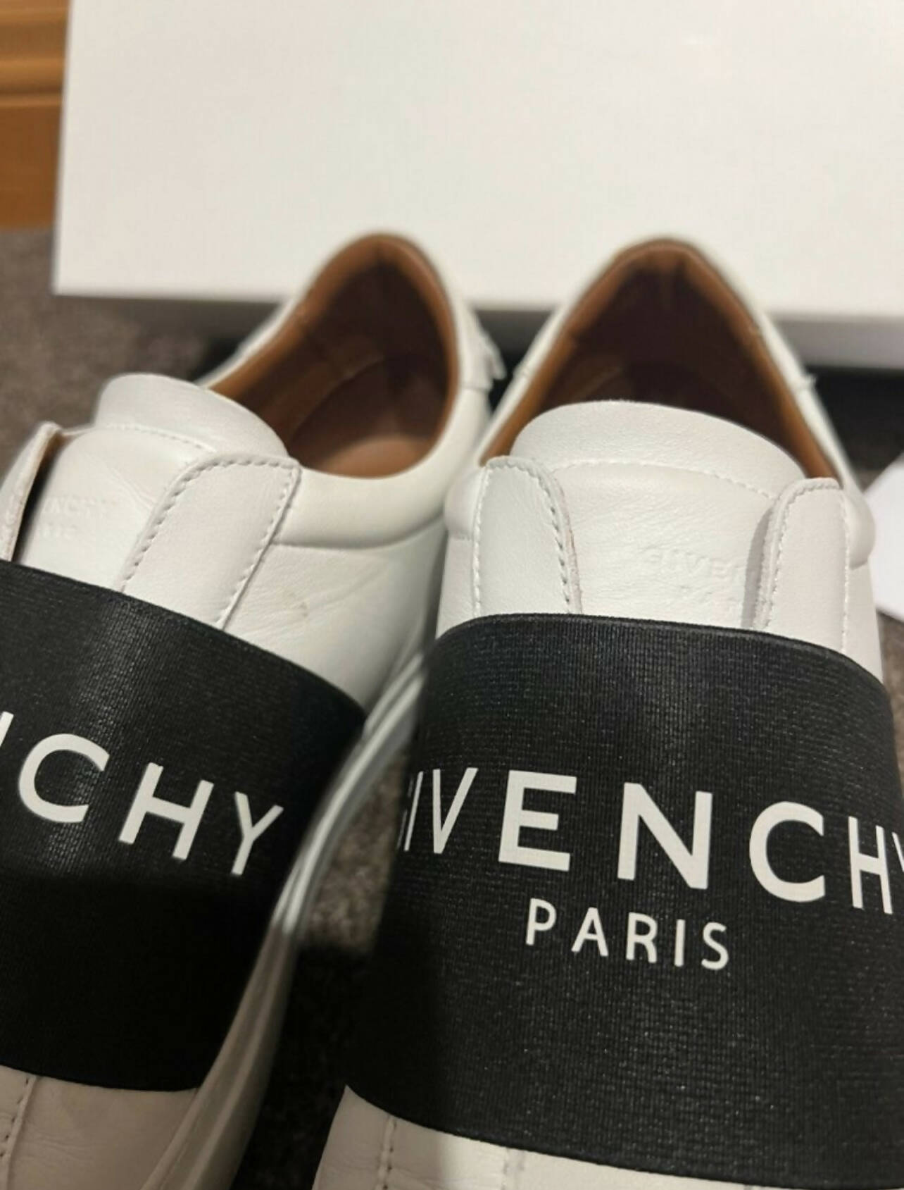 A pair of white calf leather Givenchy Urban Street Sneakers by EXCHANGE, with a wide black band featuring bold white branding across the top, displayed side by side on a brown carpet. Size 40 EU.