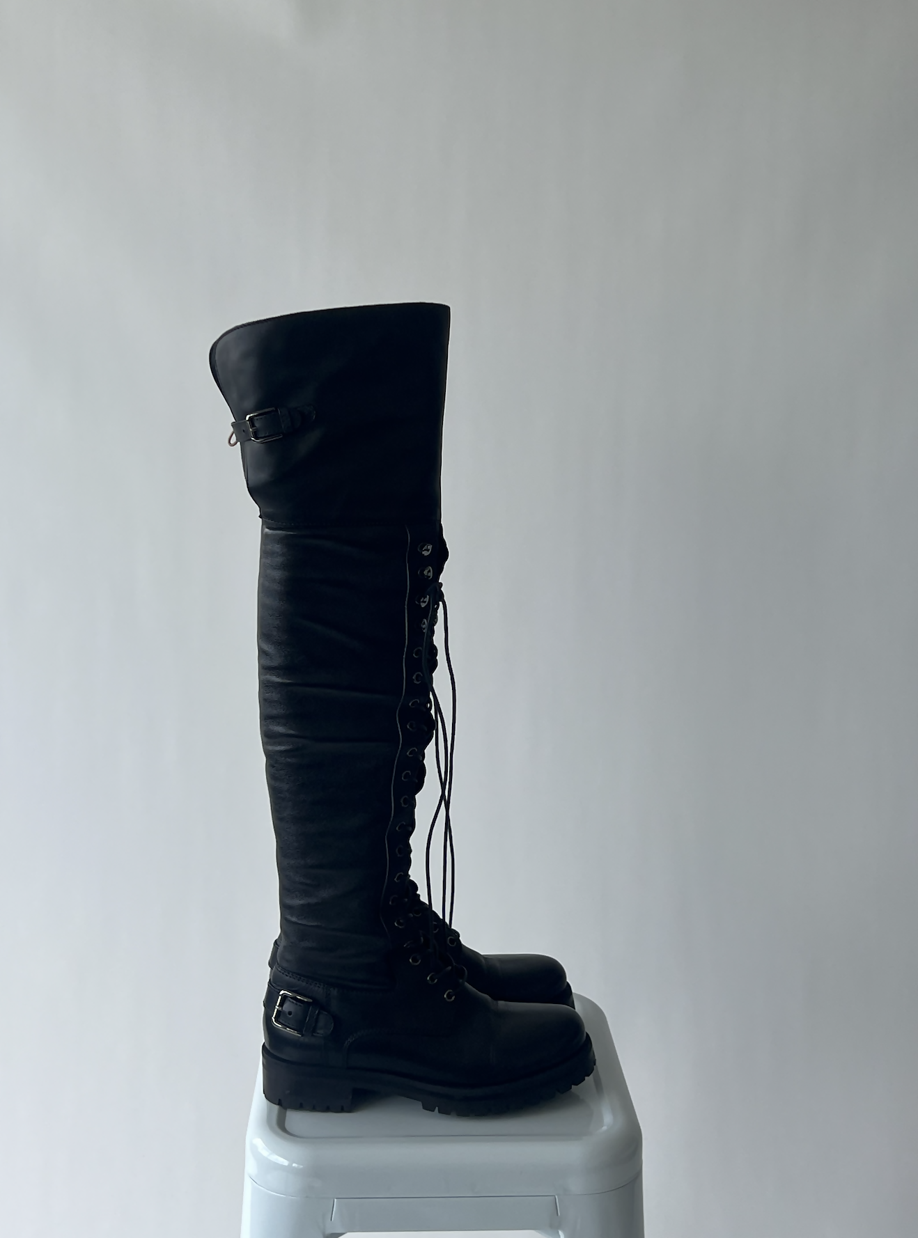 Dolce & Gabbana Thigh High Combat Boots by EXCHANGE in size 38.5, featuring tall black lace-up design with buckles, are displayed on a white stool against a light gray background.