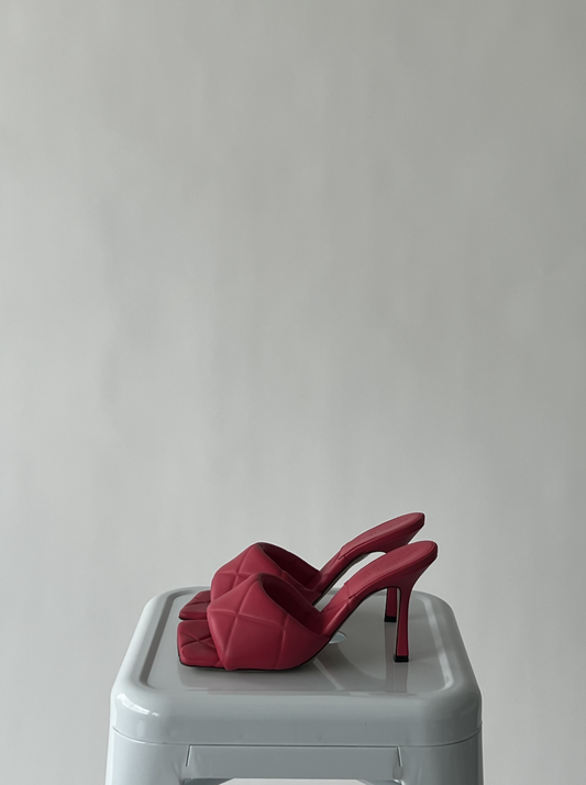A pair of Bottega Veneta Padded Leather Mules by EXCHANGE, size 38.5 with red quilted straps and open toes, rests atop a light gray square stool set against a plain light background.