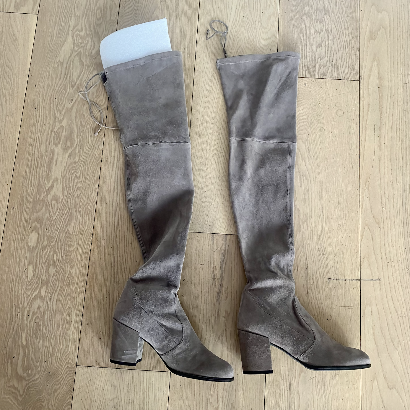 A pair of EXCHANGE STUART WEITZMAN suede thigh boots in Mushroom, size 38.5/39, with block heels and a white shaping insert, are placed side by side on a light wood floor.