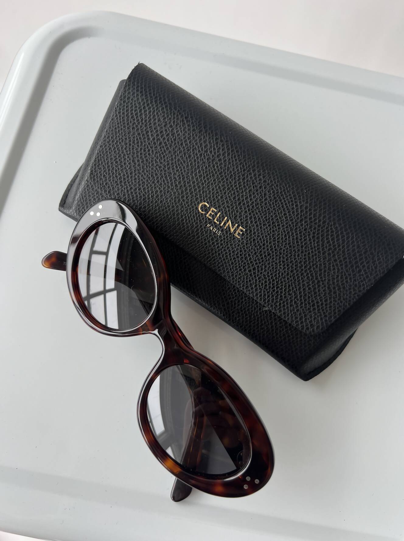 EXCHANGE Celine Glasses, barely used, are displayed beside a black textured case with gold lettering on a light gray surface.