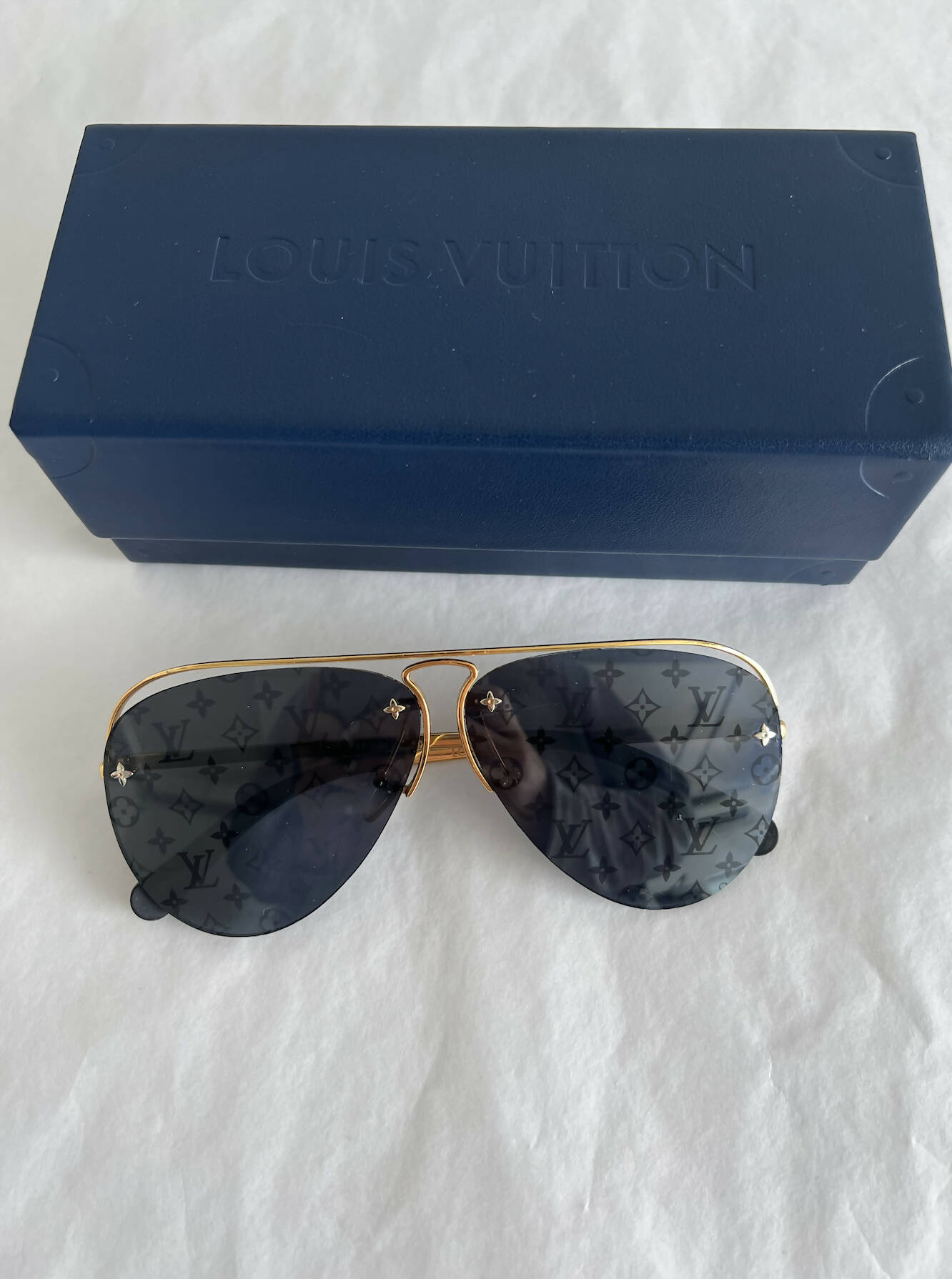 The EXCHANGE Louis Vuitton Limited Edition ClockWise Sunglasses feature gold aviator frames and monogram-patterned lenses, displayed before a blue Louis Vuitton case—ideal for collectors seeking exclusive designer eyewear.
