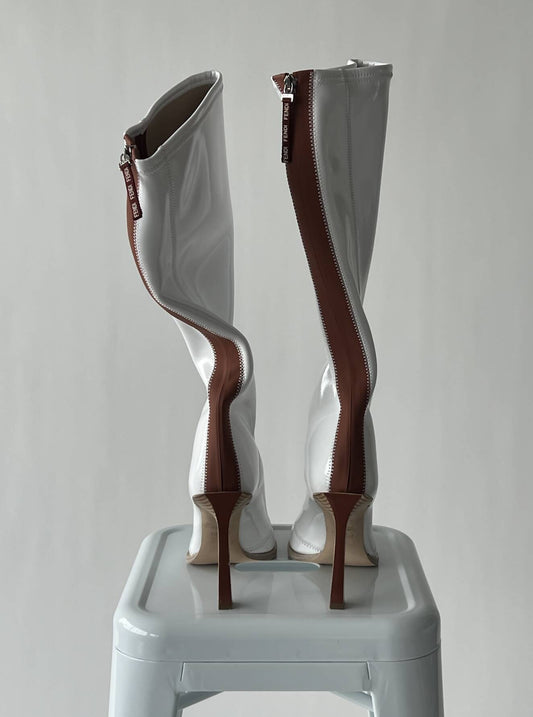A pair of EXCHANGE FENDI Glossy Neoprene FFrame Boots, size 40, featuring bold wavy brown back zippers, stands on a white stool against a plain light gray background.