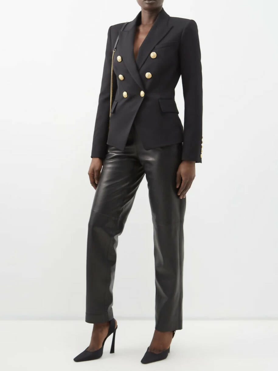 A person stands against a plain white background wearing the EXCHANGE Balmain Blazer Black, paired with black leather pants and black high-heeled shoes.