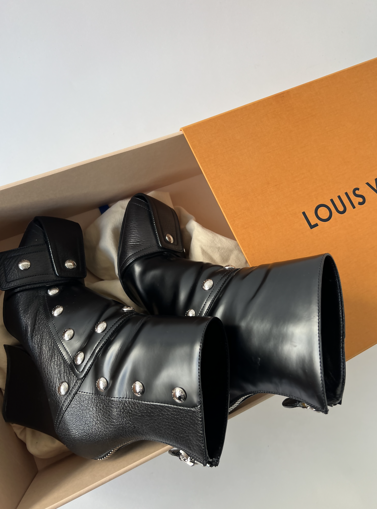 A pair of black leather ankle boots with silver studs from the EXCHANGE LV Fall Winter 2021-2022 - Full Set, inside a shoe box partially covered by an orange Louis Vuitton lid.
