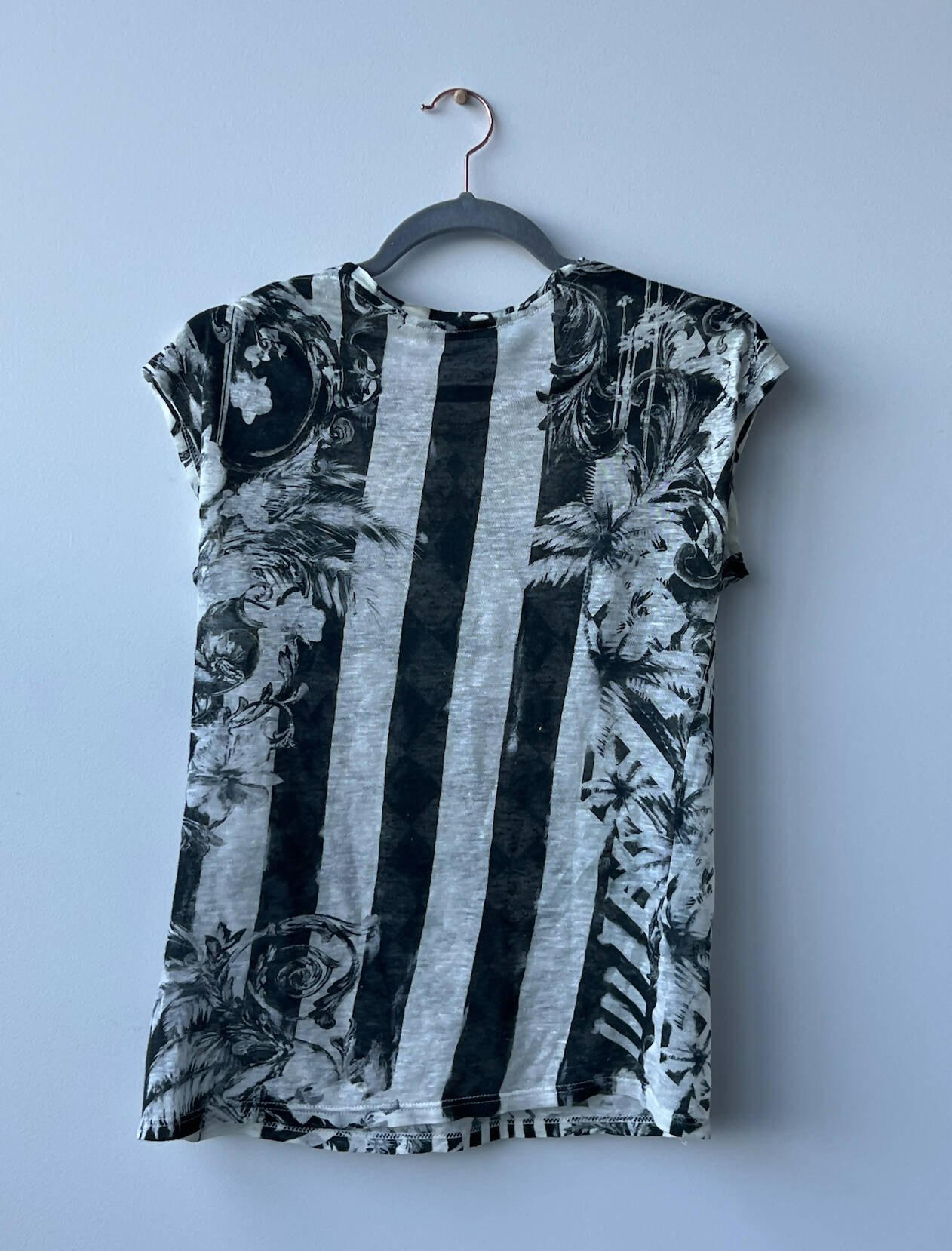 The EXCHANGE Balmain Printed Tank Top, featuring a black and white abstract floral and stripe pattern, hangs on a black hanger against a plain light gray wall—available in size 36 at exchange-store.