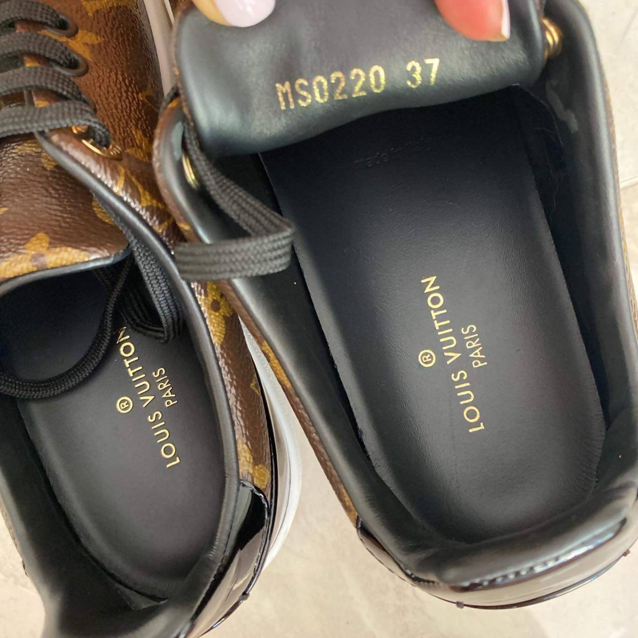 A close-up of two EXCHANGE sneakers, featuring the classic brown monogram design and black interior. The LV laces enhance elegance, with one shoe displaying code MS0220 37 on the tongue, indicating its Euro size 37 as LV FRONTROW Sneakers.