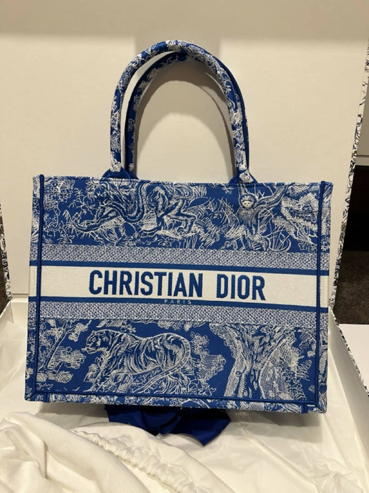 The Jess Perham Dior Book Tote Medium Dioriviera Toile De Jouy Fluorescent Blue, featuring animal and tree motifs, is displayed upright in a white fabric-lined box.